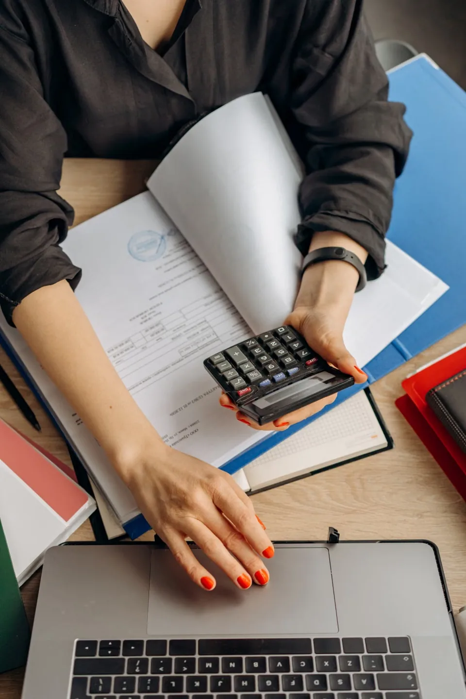 Hands reviewing financial records with a calculator and laptop